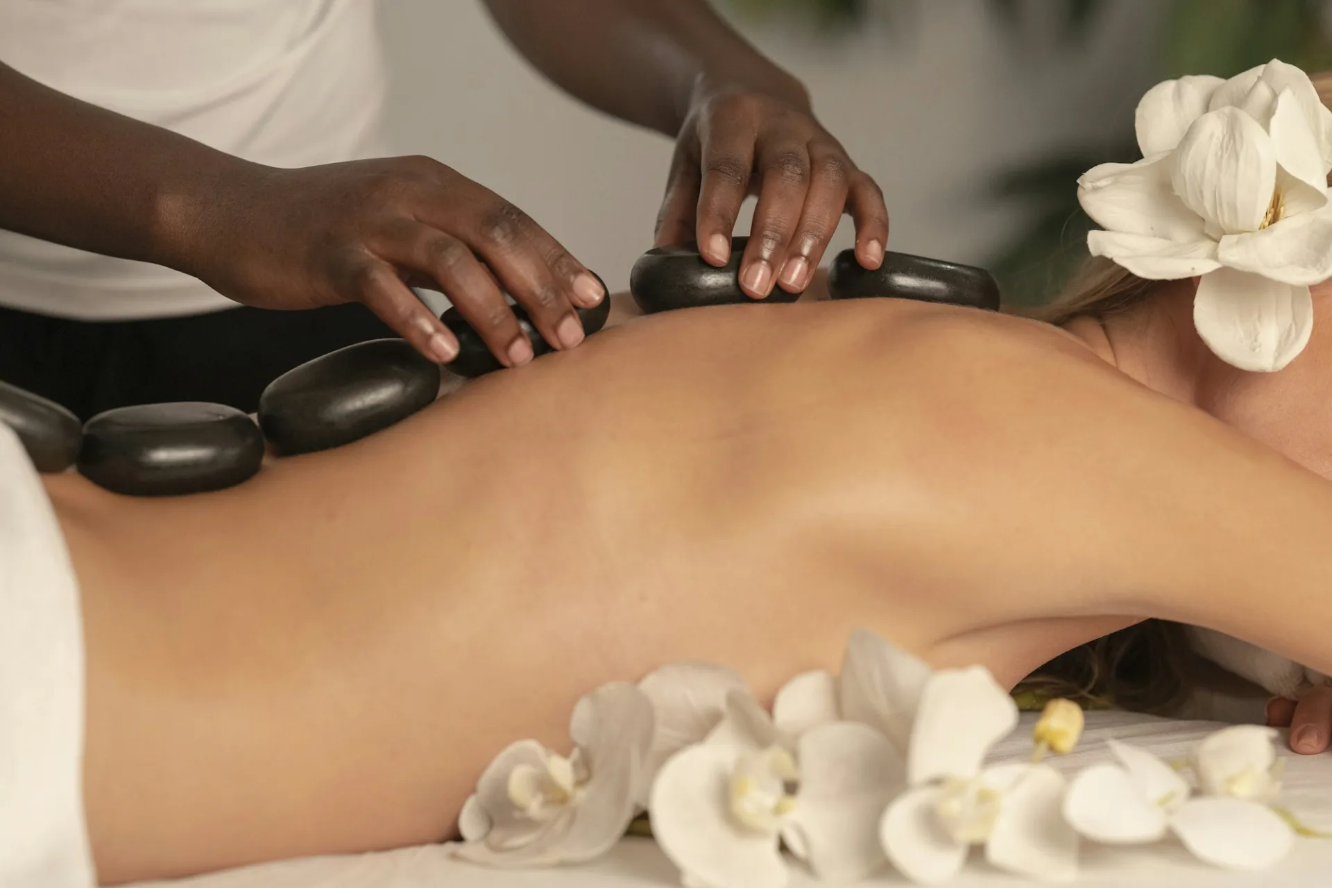 A person receiving a hot stone massage with white flowers nearby