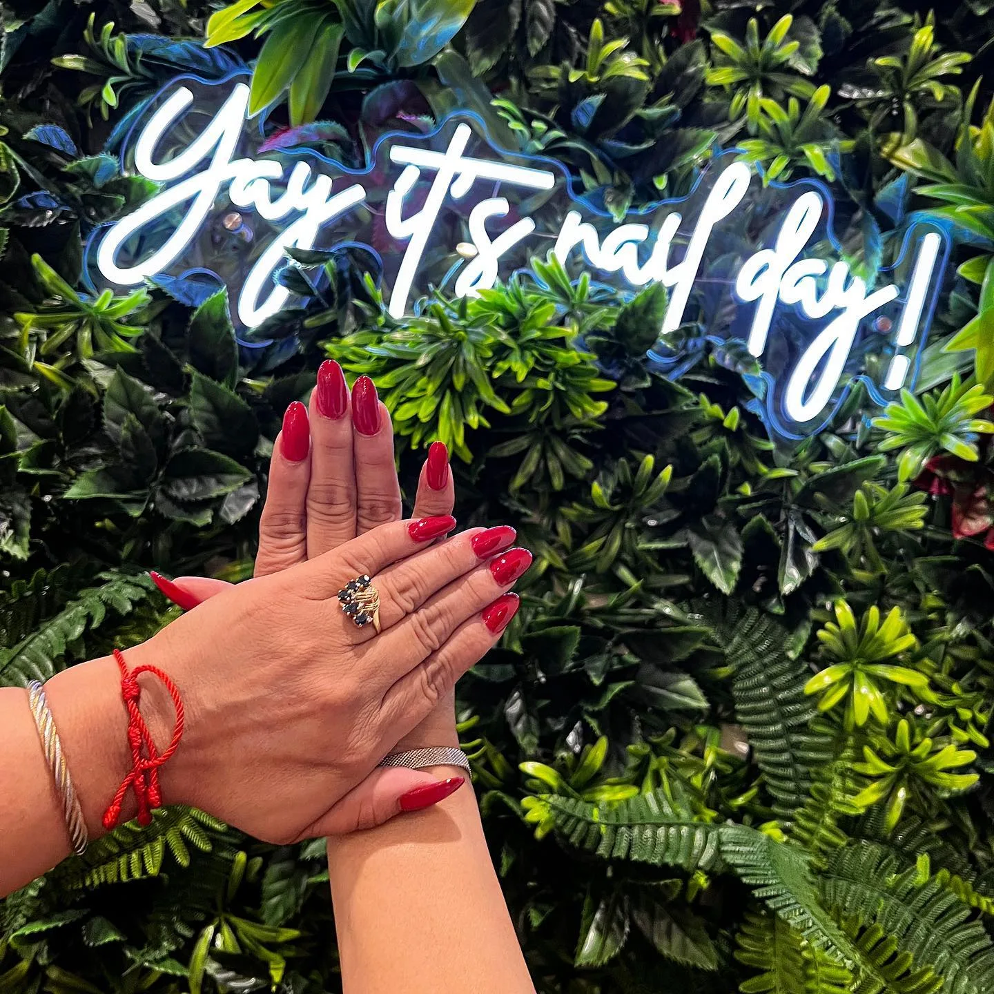 Hands with cherry red nails in front of the salon's neon sign